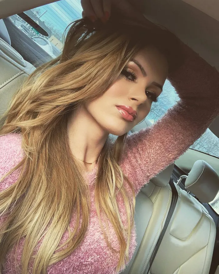 Femme blonde en tenue blanche, debout dans un salon avec des rideaux rayés
