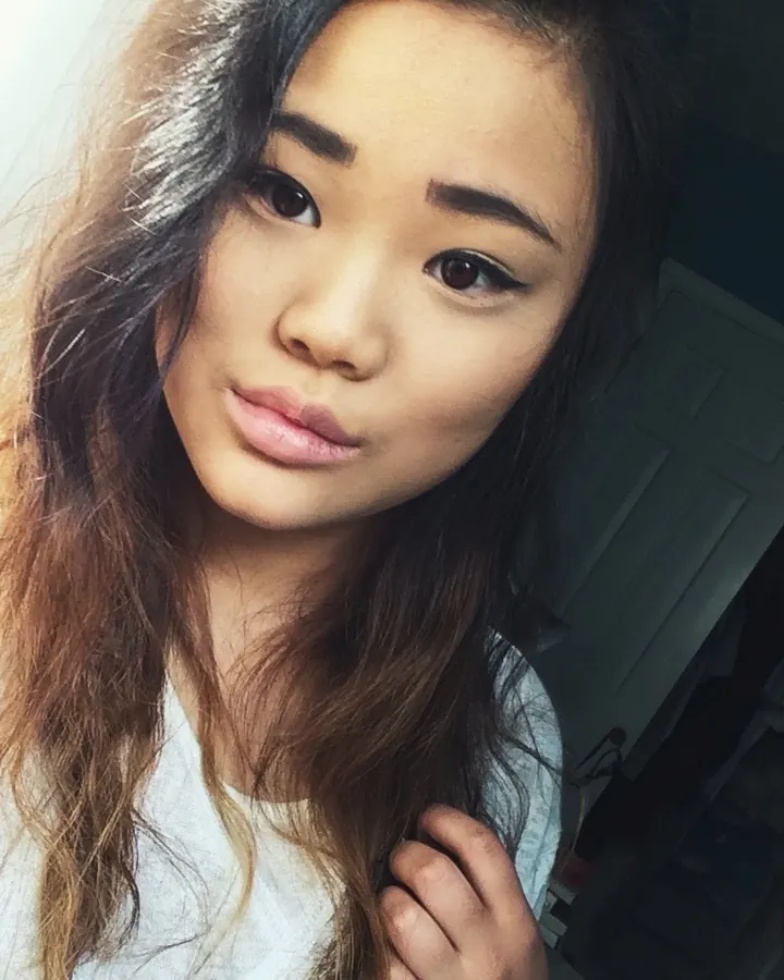 Femme aux cheveux bruns portant un haut blanc, prenant un selfie dans une chambre