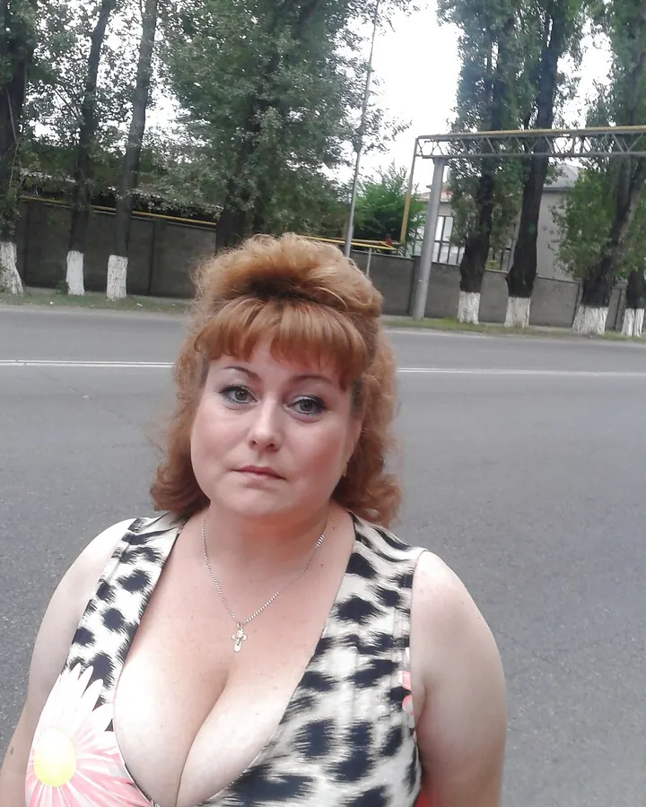 Femme aux cheveux bruns portant une robe rouge, assise sur un lit avec des couvertures rouges