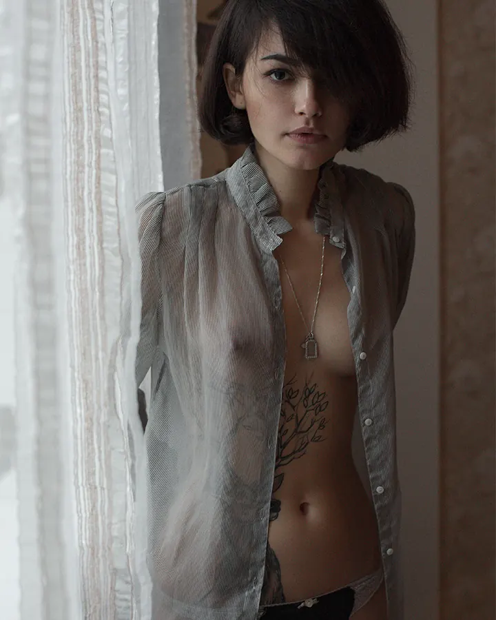 Jeune femme aux cheveux châtains regardant l'appareil photo, vêtue d'une chemise transparente et d'un sous-vêtement noir.