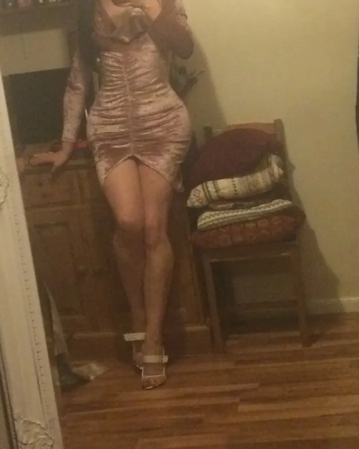 Femme aux cheveux bruns foncés, souriante, prenant un selfie, en robe rose or, devant un miroir.