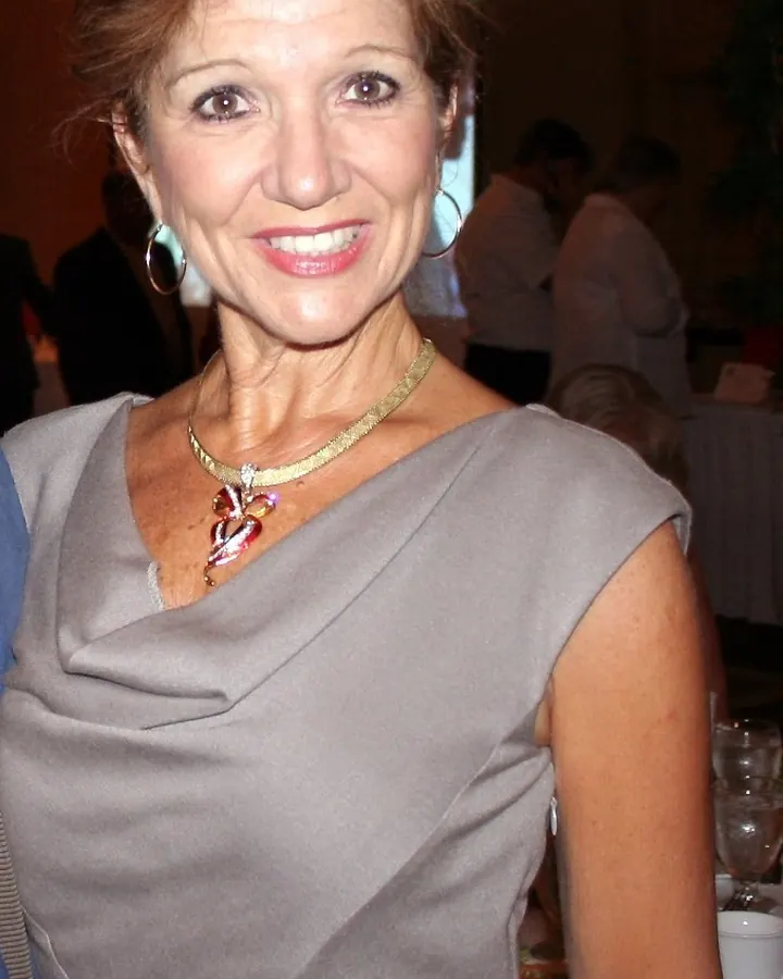 Femme mûre en robe grise élégante, collier doré, sourire chaleureux, ambiance de soirée