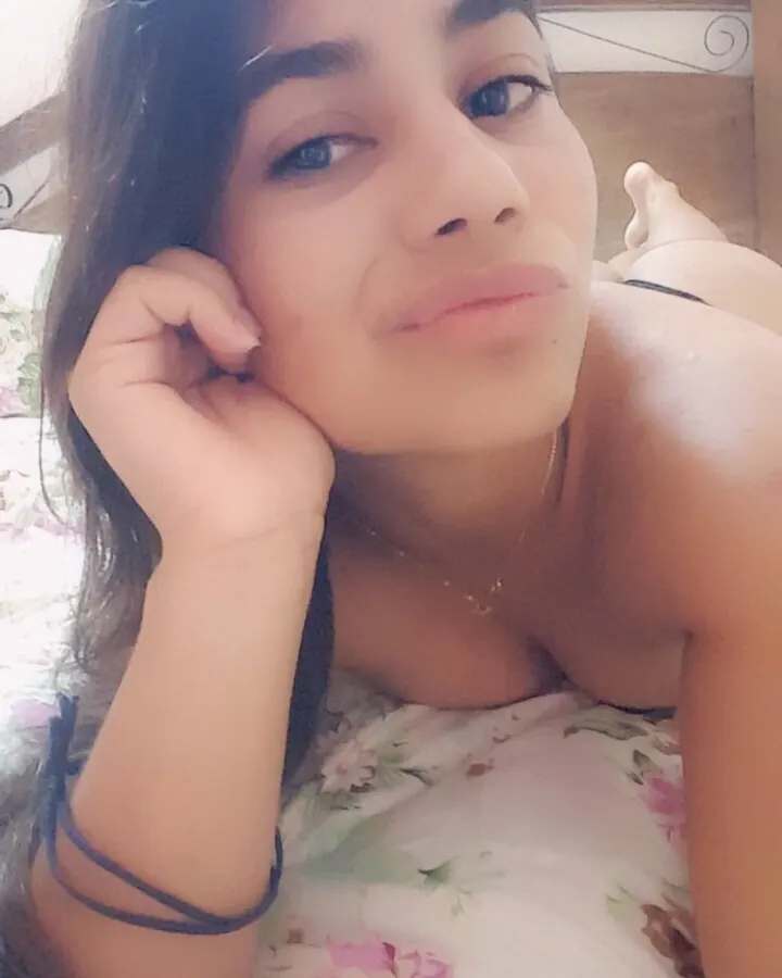 Femme arabe en chemise fleurie, allongée, main près de l'oreille, regard direct, ambiance intime