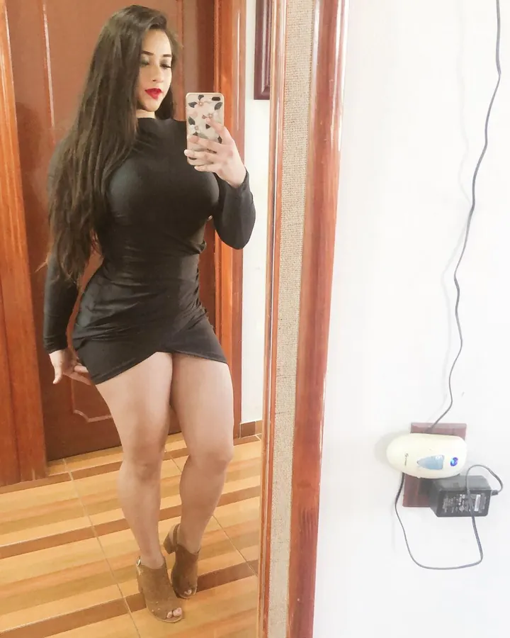 Femme aux cheveux châtains, en robe noire, posant près d’un canapé