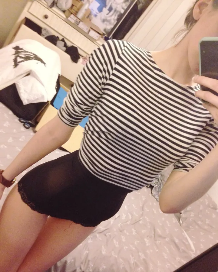 Jeune femme aux cheveux châtains prenant un selfie dans un miroir, portant un haut rayé noir et blanc et une jupe noire