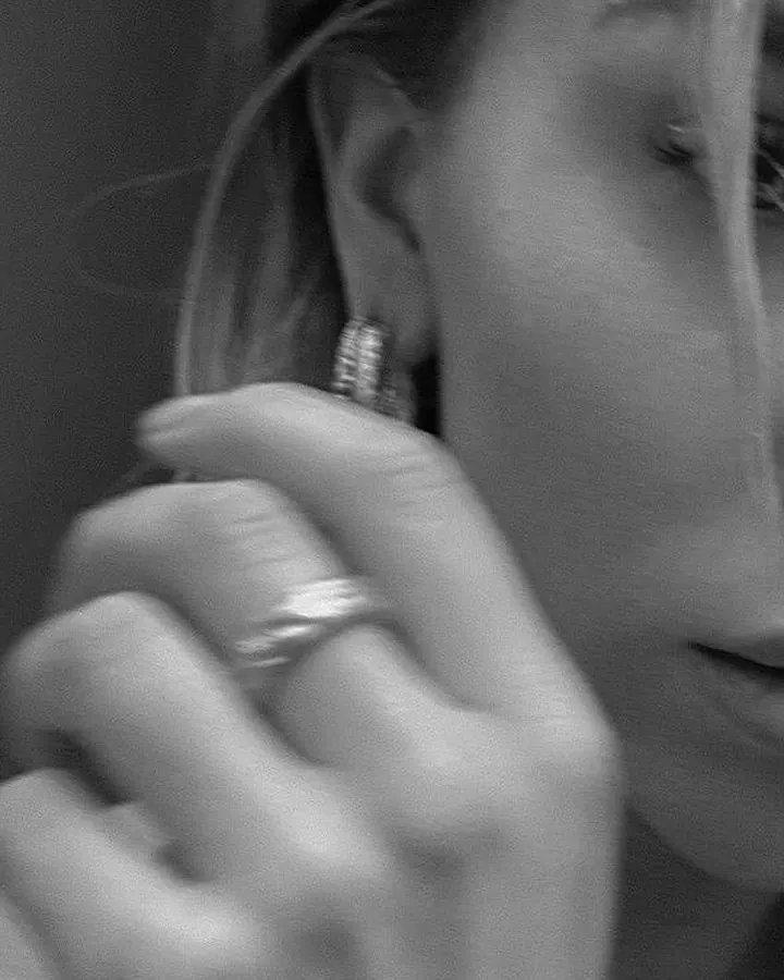 Photo en noir et blanc d'une femme touchant son oreille avec une main ornée d'un anneau, un regard intense.