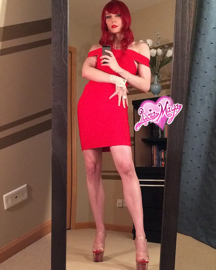 Femme aux cheveux roux portant une robe rouge, prenant un selfie devant un miroir dans une chambre.