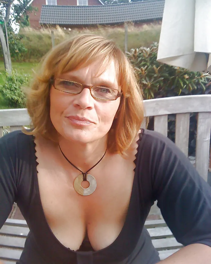Femme mûre aux cheveux blonds, portant des lunettes, en haut noir, assise sur une terrasse.
