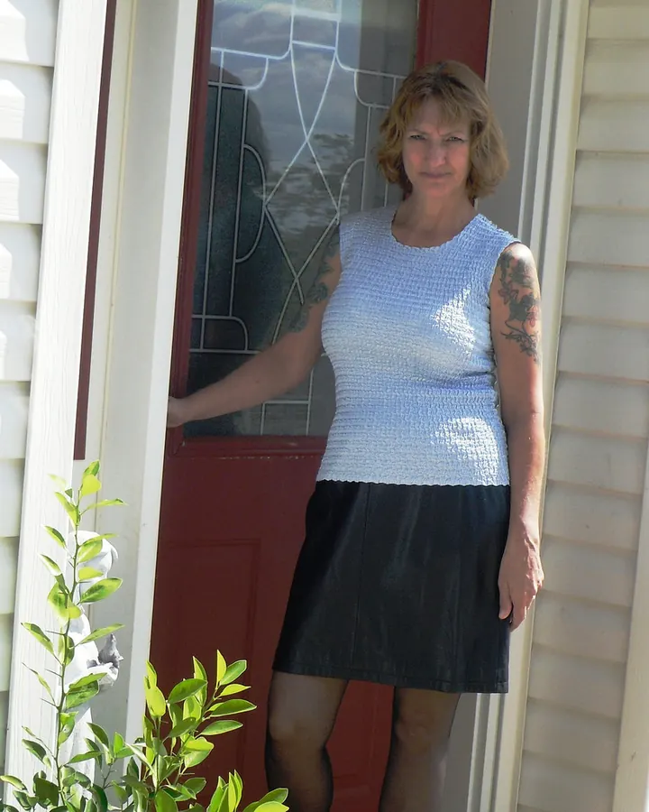 Femme blonde en haut bleu, bras tendu vers une porte