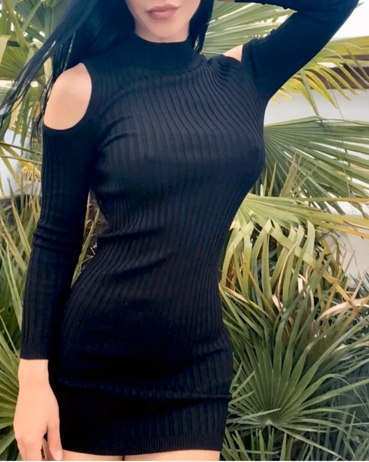 Femme en robe noire, posant devant des plantes tropicales, les mains sur les hanches.