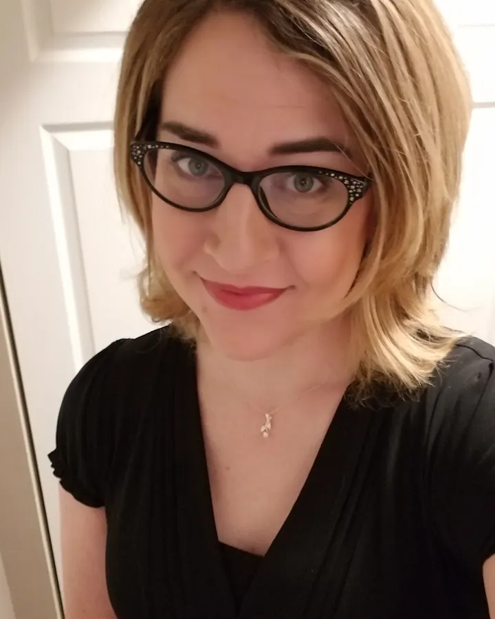 Femme souriante portant des lunettes, vêtue d’un haut noir, regardant l'appareil photo avec un léger sourire.