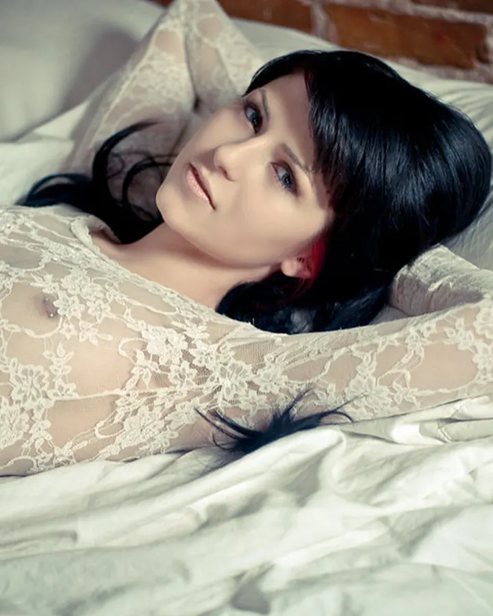 Femme allongée sur un lit en dentelle blanche, regardant vers le haut avec une expression sereine.