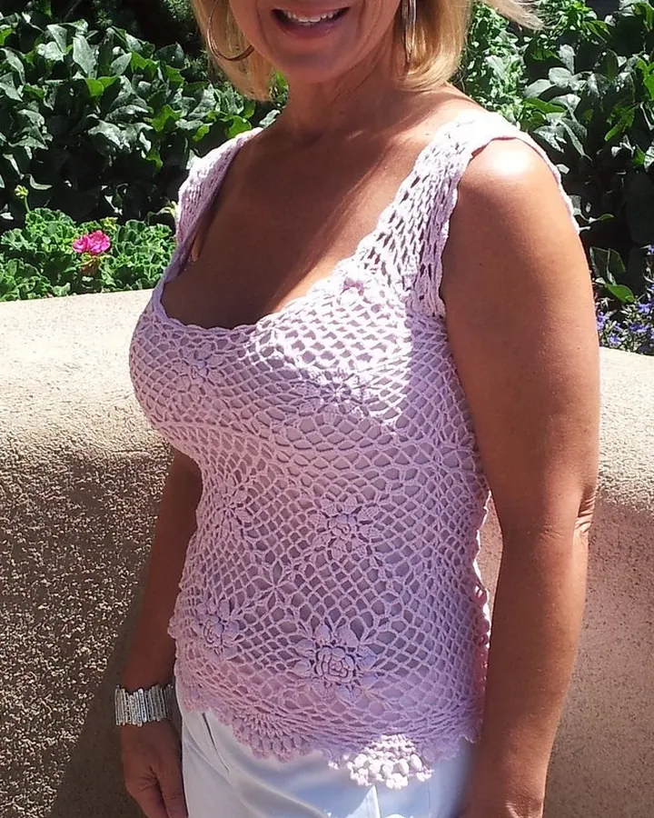 Femme souriante en tenue d’été, portant un haut tricoté rose et un short blanc, dans un jardin.