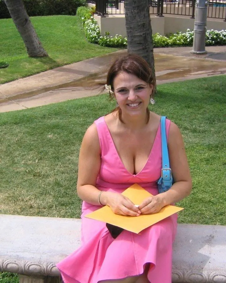 Femme souriante en robe rose, assise sur un banc dans un parc, tenant un papier jaune.