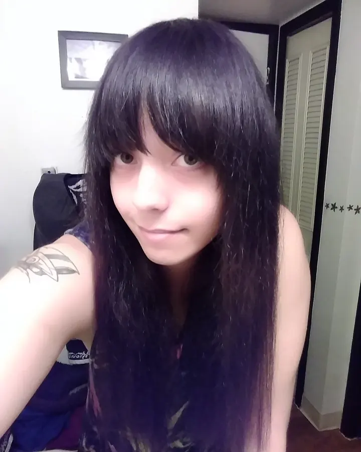 Femme aux cheveux bruns-noirs, prenant un selfie dans une pièce, regardant l'appareil.