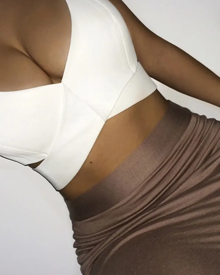 Femme aux cheveux bruns, en haut blanc, posant contre un mur
