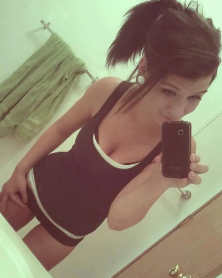 Jeune femme aux cheveux bruns, prenant un selfie dans un miroir de salle de bain