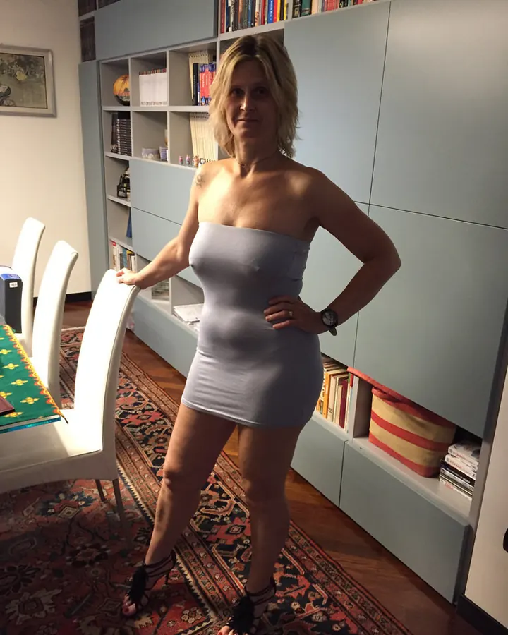 Femme blonde aux yeux gris, en robe bleue, posant avec un sourire chaleureux devant un décor festif.