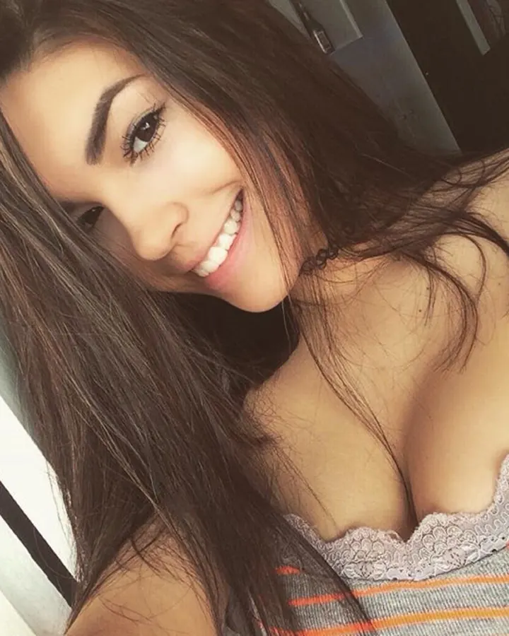 Femme aux cheveux bruns, en tenue colorée, prenant un selfie dans une pièce intérieure.