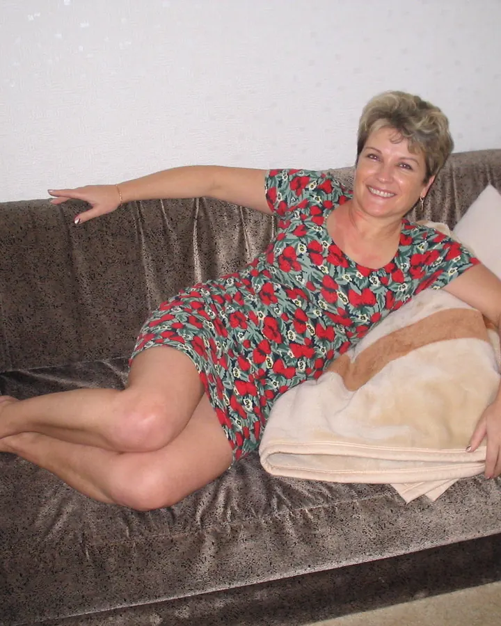 Femme blonde aux cheveux courts, en robe blanche, souriante, dans un cadre intérieur élégant.