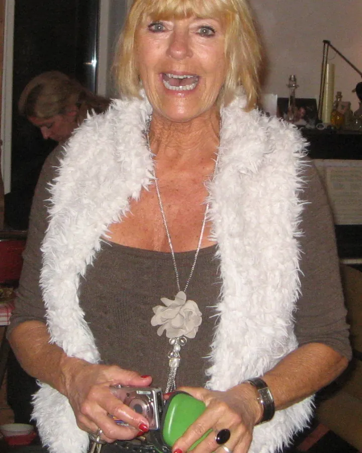 Femme blonde aux cheveux courts, en robe blanche, souriante, dans un cadre intérieur élégant.