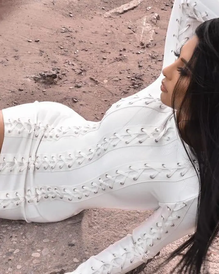 Femme aux cheveux noirs, en combinaison blanche à lacets, allongée sur un sol terreux.