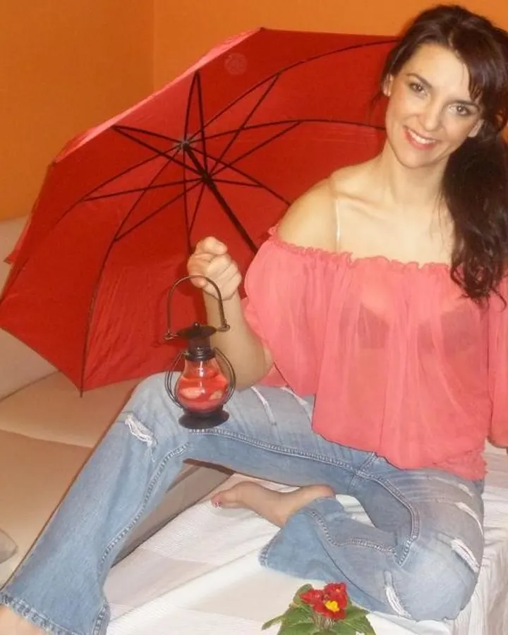 Femme brune en tenue légère, assise sur un canapé avec un parapluie rouge et une lanterne