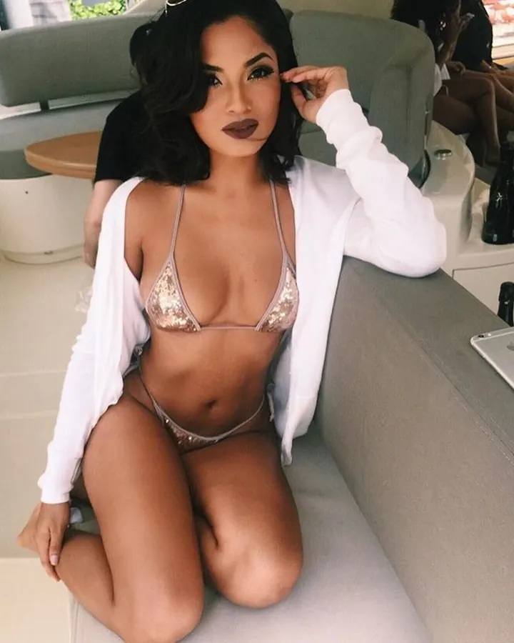 Femme noire en bikini doré, assise sur un bateau, avec une veste blanche ouverte.