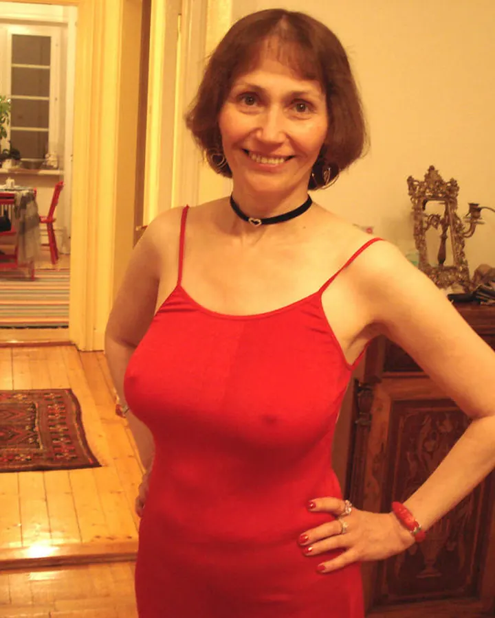 Femme en robe rouge, posant dans un couloir avec un meuble en bois sculpté.