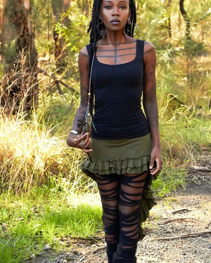 Femme africaine aux dreadlocks, tatouages, tenue noire et verte, en forêt