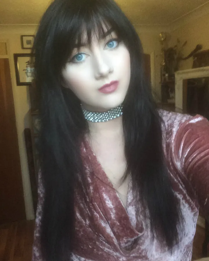 Femme aux cheveux bruns portant un haut noir, se tenant de profil dans un couloir, regardant l'appareil.