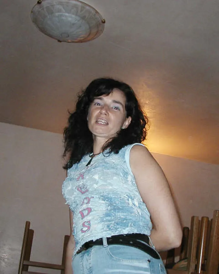 Femme aux cheveux bruns-noirs, en haut noir, posant dans une chambre.