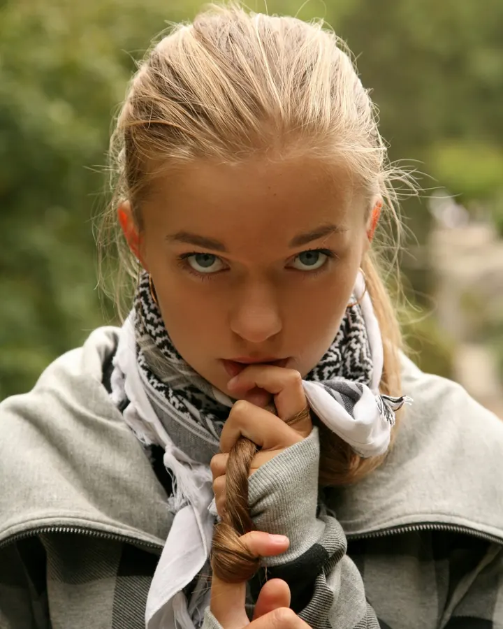 Femme aux cheveux blonds en haut noir, jupe en jean courte, veste en cuir noir, chaussures noires, appuyée sur une voiture argentée la nuit.
