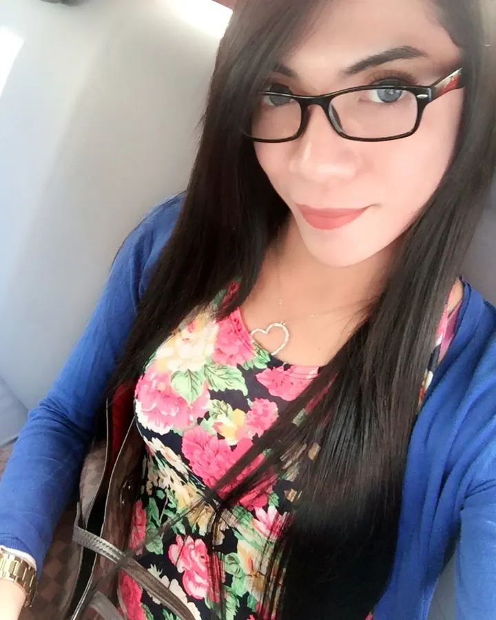 Femme aux cheveux noirs portant lunettes, chemisier fleuri sous cardigan bleu, sourire discret