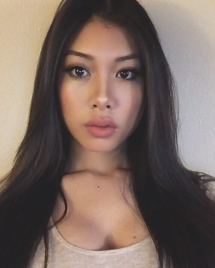 Femme aux cheveux noirs, yeux sombres, regard fixe, haut clair, fond neutre