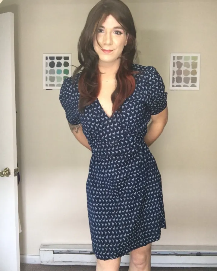 Femme brune en robe bleue à motifs, mains dans le dos