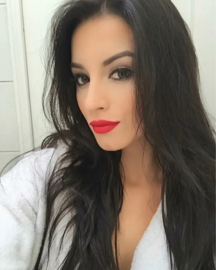 Femme aux cheveux noirs, maquillage marqué, rouge à lèvres rouge, portant un peignoir blanc, regardant l'appareil.