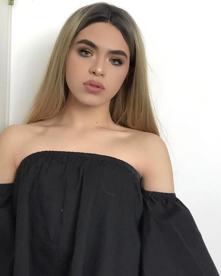 Jeune femme aux cheveux blonds platine, en haut noir décolleté, regardant directement l'objectif