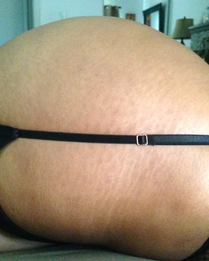 Plan rapproché du derrière d'une femme portant un string noir et des collants résille, allongée sur un canapé.